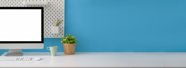 Close up view of creative workspace with blank screen computer, mug, tree pot and copy space