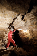 Man walking and exploring dark cave with light headlamp underground. Mysterious deep dark, explorer discovering mystery moody tunnel looking on rock wall inside.