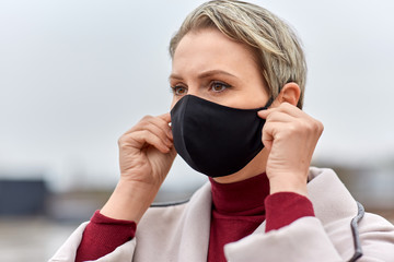 health, safety and pandemic concept - young woman wearing black face protective reusable barrier mask outdoors