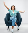 © Syda Productions - comfort, people and furniture concept - portrait of happy smiling young woman in turquoise shirt and jeans sitting in modern armchair over grey background