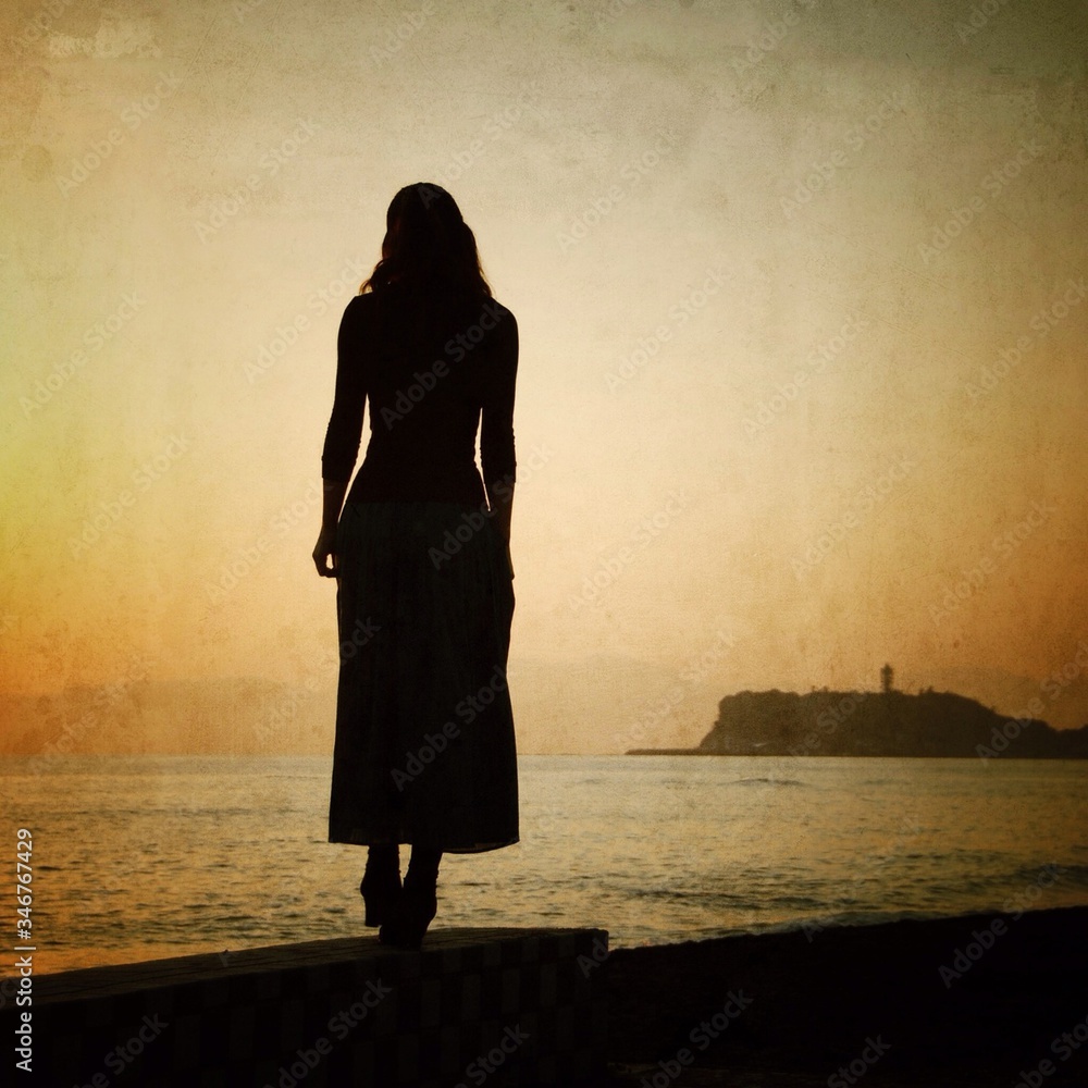 Rear View Of Silhouette Woman Standing On Retaining Wall By Sea - obrazy, fototapety, plakaty 