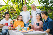 © linghaa - Happy big family have a lunch at outdoor in green garden. Lunch or tea time on picnic table in summer. Old woman make a bread with Fruit jam to give husband.  Big family outdoor lunch concept.