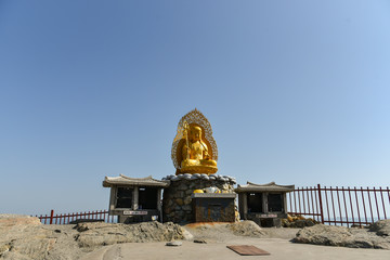 Wall Mural - Busan city, South Korea - NOV 01, 2019: Chinese culture golden Buddha sculpture that standing on the respective shrine near Haedong Yonggung Temple.