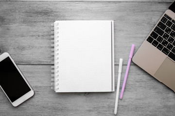 White notebook, two pens, laptop and phone on a white wooden table top view of flat objects