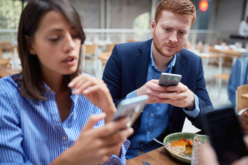 Wall Mural - Young man and woman at business lunch texting message.