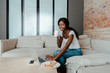 © LIGHTFIELD STUDIOS - African american freelancer with cup of tea smiling and using laptop at coffee table with smartphone and plate with toasts in living room