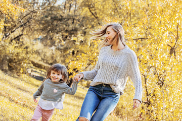 Beautiful woman and her little daughter holding hands and running in autumn park. Tiny girl having fun and playing with her young mother outdoors. Happy family relationships of mom and child