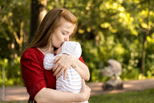 A young mother with a small newborn in her arms in a summer park. Happiness Maternity, Recovery Postpartum Concept