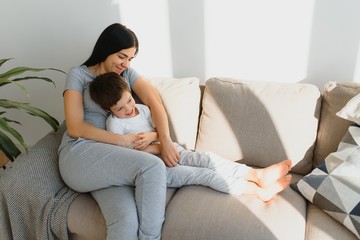 Young mother with her 4 years old little son dressed in pajamas are relaxing and playing in the bed at the weekend together, lazy morning, warm and cozy scene.