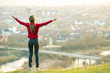 © bilanol - Young woman standing outdoors raising her hands enjoying city view. Relaxing, freedom and wellness concept.