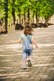 Fototapeta Młodzieżowe - May 2020. Kiev Ukraine. A little girl plays outside in a park, collects plants on a sunny day in denim overalls and a T-shirt with a print  LOL