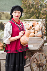 Beautiful girl in national dress. Holding an ancient pot in his hands. Antique clothing of the late 19th century. Beautiful dress and skirt on a woman. The concept of rural life, national traditions