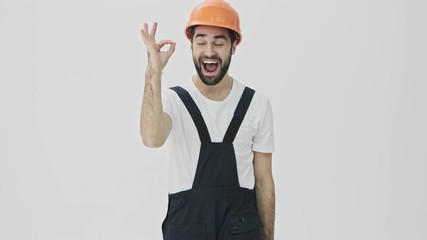 Sticker - Cheery positive young bearded man builder isolated over white wall background in helmet showing okay gesture.