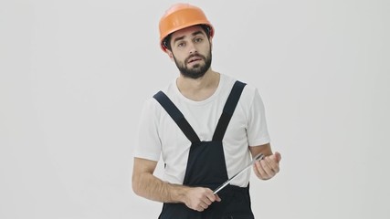 Sticker - Concentrated young bearded man builder isolated over white wall background in helmet with wrench