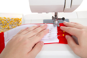 Close up of hands make surgical style face mask with filter pocket out of bright red and white cotton fabrics on a well used sewing machine. Isolated on white.