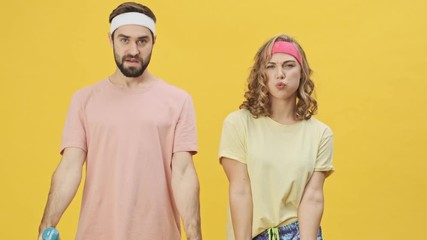 Sticker - An attractive young athletic couple man and woman in sportswear is doing exercises lifting dumbbells isolated over a yellow background in studio