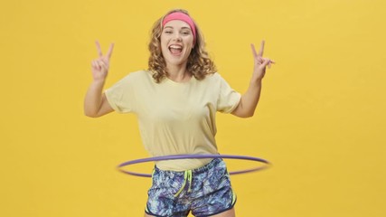 Poster - A happy smiling young athletic woman in sportswear is spinning the wheel isolated over a yellow background in studio