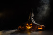 Spooky orange pumpkins for Halloween stand in a row on a dark background. Jack O Lantern in a witch hat. Mystical fog creeps on the ground. Trick or treat.