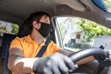 Young man in black mask driving a car and wearing yellw t-shirt, headphones and gloves. Tje hands of man holding the wheel of a vehicle. Safety of virus concept