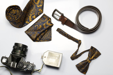 Retro camera with flash. Photographer accessories: belt, bow-tie and tie. Shot from above, on a white background.