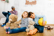© Westend61 - Brother and  sister sitting in playroom with cuddly toys, father in background