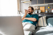 © Westend61 - Portrait of smiling man sitting on couch at home using mobile phone
