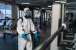 © sutulastock - Cleaning and Disinfection in crowded places amid the coronavirus epidemic Gym cleaning and disinfection Infection prevention and control of epidemic. Protective suit and mask and spray bag COVID-19