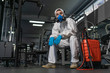 © sutulastock - Cleaning and Disinfection in crowded places amid the coronavirus epidemic Gym cleaning and disinfection Infection prevention and control of epidemic. Protective suit and mask and spray bag COVID-19