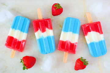 Red, white and blue summer fruit ice pops. Top view on a white marble background.