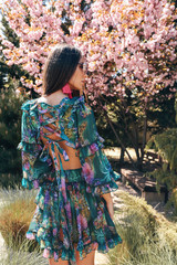 beautiful sensual woman with dark hair in luxurious dress with floral print  and accessories posing in summer garden