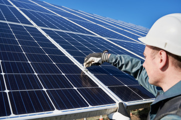 Wall Mural - Close up of man technician mounting blue photovoltaic solar panel. Solar installer wearing safety helmet and gloves. Concept of alternative energy and power sustainable resources.