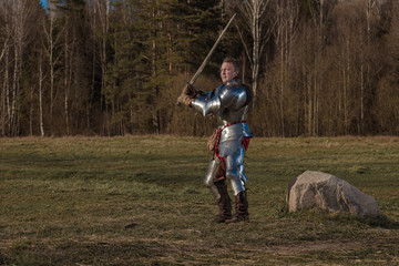 A knight on foot in armor and holding a sword in his hands shows combat attacks on the battlefield.