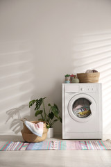 Poster - Modern washing machine and wicker basket with laundry near white wall. Interior design