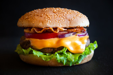 Burger with cheese, bacon, tomato and lettuce on dark wooden background