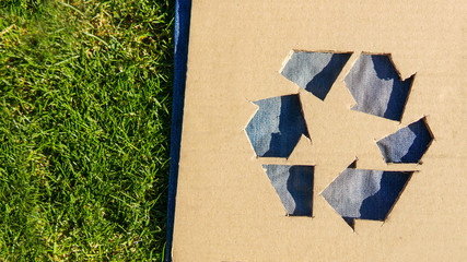 Wall Mural - Recycle symbol on denim fabric over green grass. New skirt from old boyfriend jeans