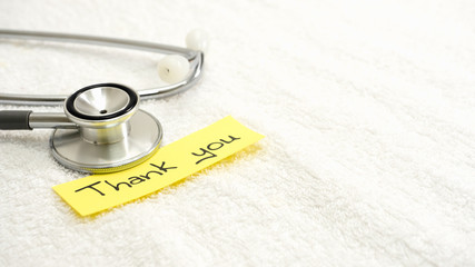 Black doctor thanks message On a yellow paper The background is white cloth. There are stethoscope doctors besides. There is a copy space.