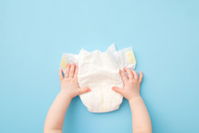 Baby Hands Touching White Diaper On Light Blue Table Background. Pastel Color. Closeup. Point Of View Shot. Top Down View.
