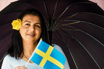 Wall Mural -  Woman with umbrella holds flag of Sweden in front of isolated wall background