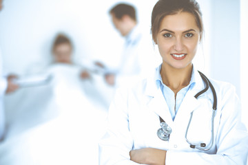 Wall Mural - Female doctor smiling on the background with patient in the bed and two doctors