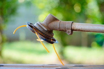 Close up trimmer head equipment with yellow nylon line cutting grass.