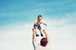 © guas - Happy father throwing his son child into the air, carefree having fun outdoors over the blue sky background, family and father's day - concept