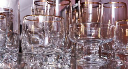 Glass cups arranged and hanging from a bar shelf with background light in the darkness. Wine, beer and other drinks glassware concept.