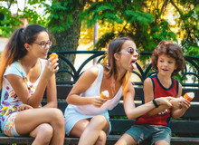 Happy Family Eating Ice Cream In A Summer Park. Sisters And Little Brother Have Fun. Walk In The Green Park