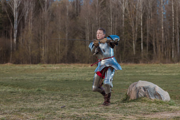 A knight on foot in armor and holding a sword in his hands shows combat attacks on the battlefield.