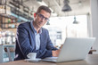 © weyo - Young entrepreneur wearing glasses looks at the camera during a coffee break in a cafe with a computer in front of him