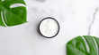Jar with moisturizer skin cream and tropical monstera leaves on marble background. SPA natural organic cosmetic product. Skincare and body treatment concept.