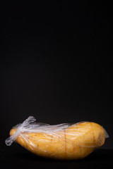 Wall Mural - Vertical frame of plastic packed large yellow sweet potato. Studio low key food still life contrasted against a dark background.