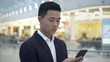 © diproduction - Portrait of asian young businessman black hair dressed in suit drinking coffee holding phone standing on background of lights in mall