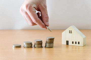 Men hand put coin into stack beside wood house , coin stack on wood table. Saving plan to buy property.