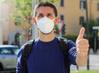 © zigres - COVID-19 Positive young man wearing protective mask KN95 FFP2 avoiding Coronavirus disease 2019 showing thumbs up in city street